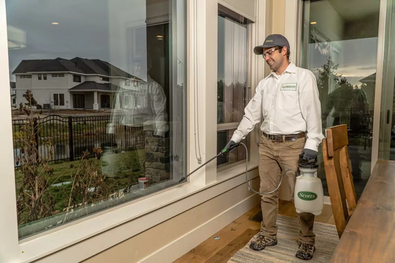 Green Pest Management technician spraying interior home Green Pest Management exterminator spraying a window sill