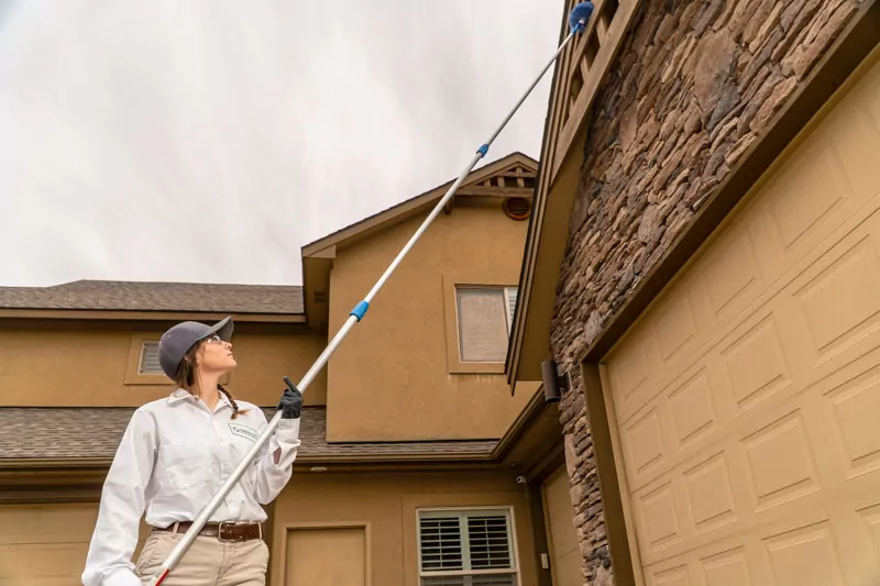 Green Pest Management exterminator performing a de-webbing and wasp control service on a home