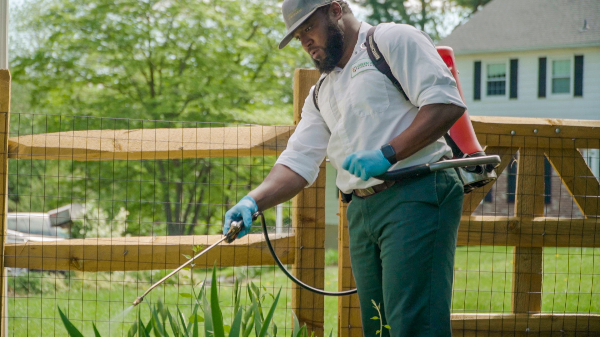 Green-Pest-Management-vid-still-3 Pest control technician spraying for pests around home